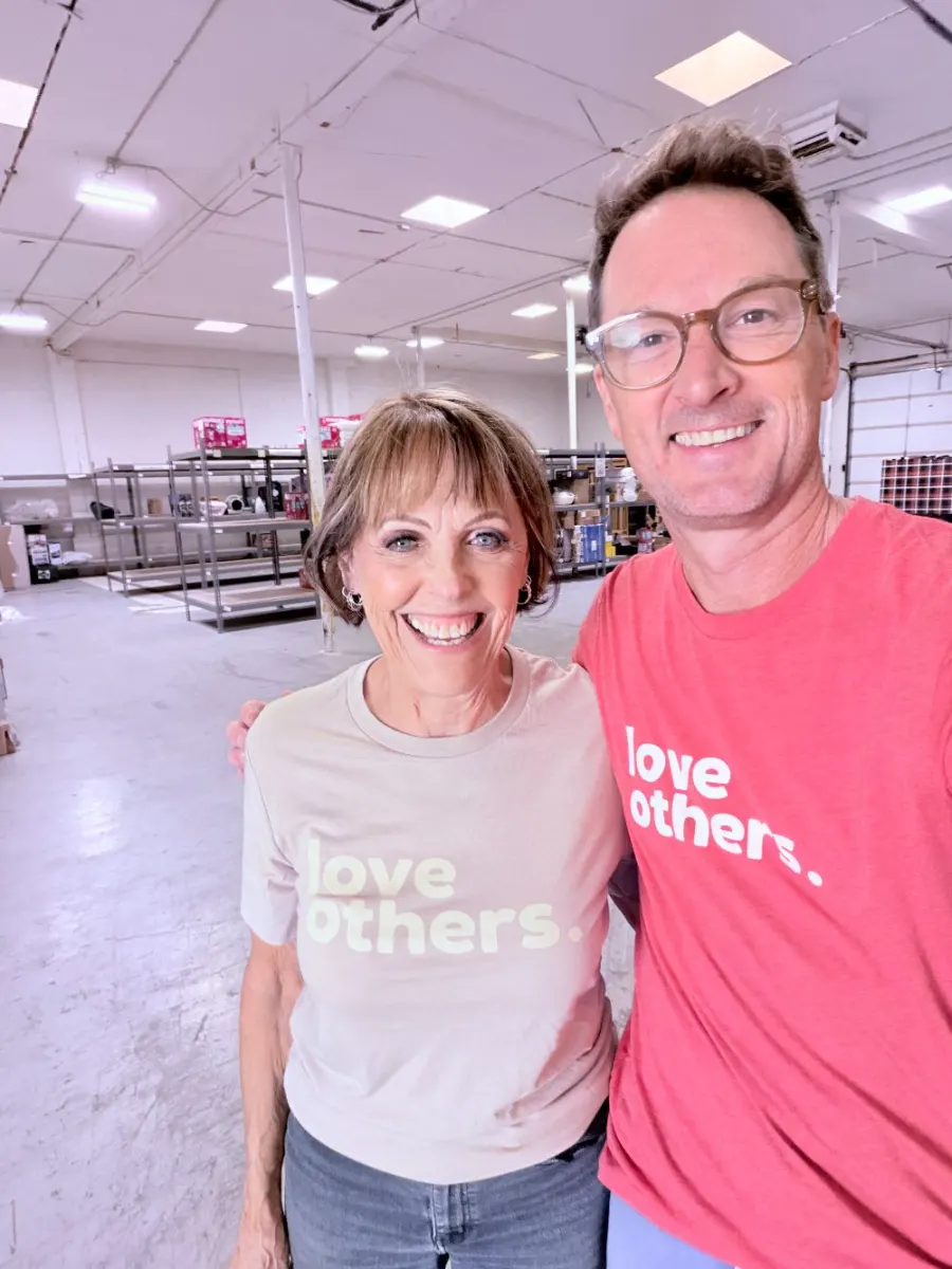 Two Capital Cares team members in love others. shirts in the warehouse